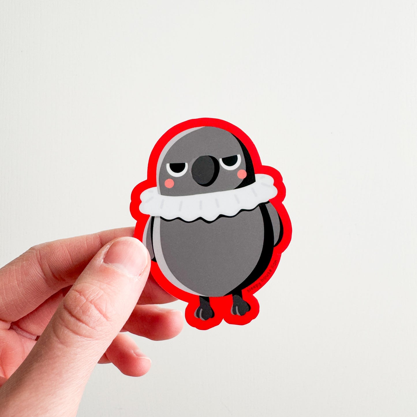 Hand holding a cartoon crow sticker with a red border on a light gray background