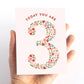 Hand holding a card with floral number '3' and text 'TODAY YOU ARE 3' on a white background