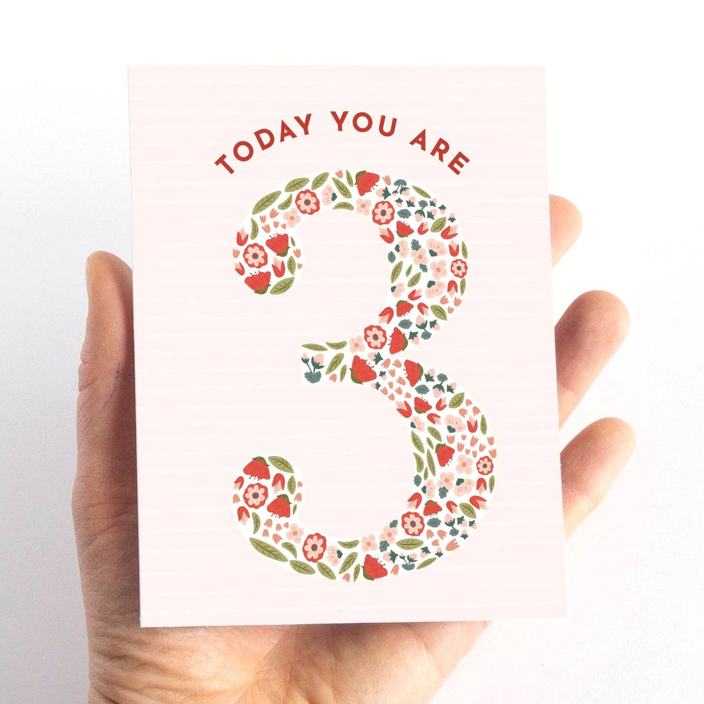 Hand holding a card with floral number '3' and text 'TODAY YOU ARE 3' on a white background