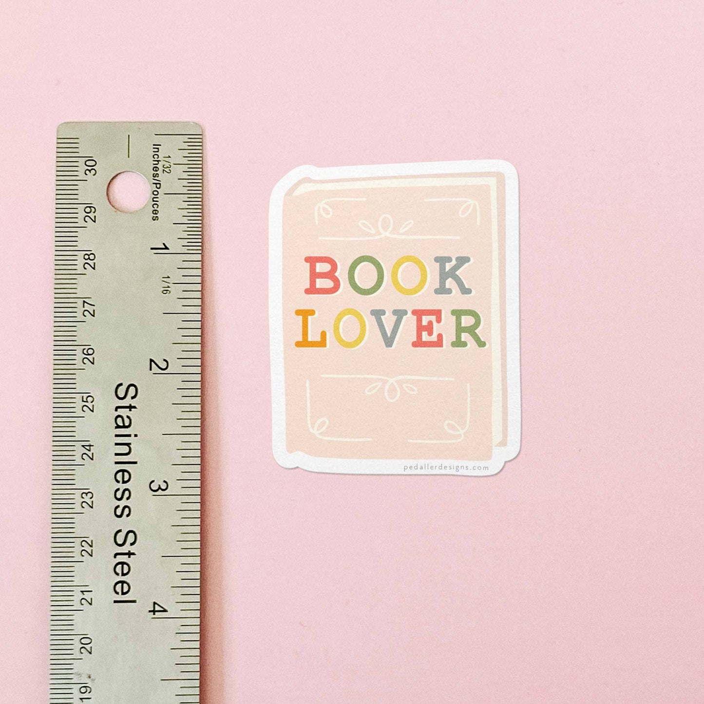 Sticker with 'BOOK LOVER' text next to a ruler on a pink background