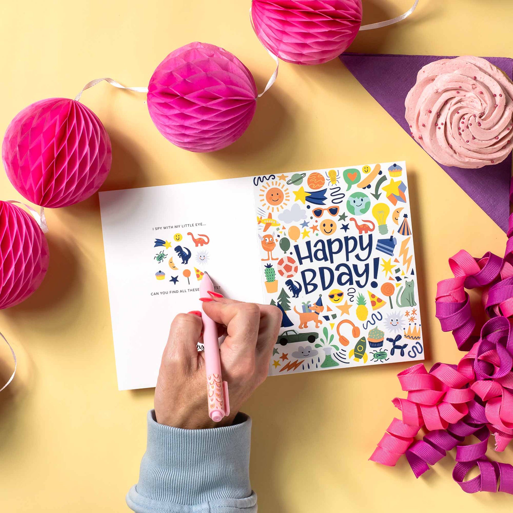 Hand writing on a birthday card with decorative elements on a yellow surface