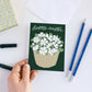 Hand holding a 'Happy Easter' card with floral design on a white surface with stationery items.