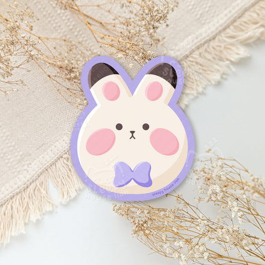 Cute cartoon bunny face sticker with a purple bow on a neutral background